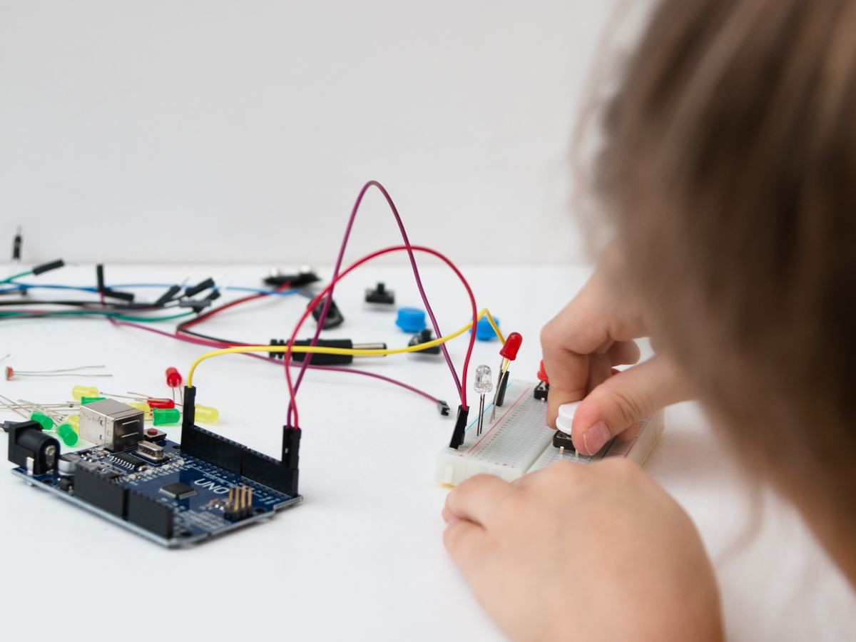 A cute girl constructs robot arduino and program it. The boards and microcontrollers are on the table. STEM education. Programming. Mathematics. The science. Technologie. DIY. 